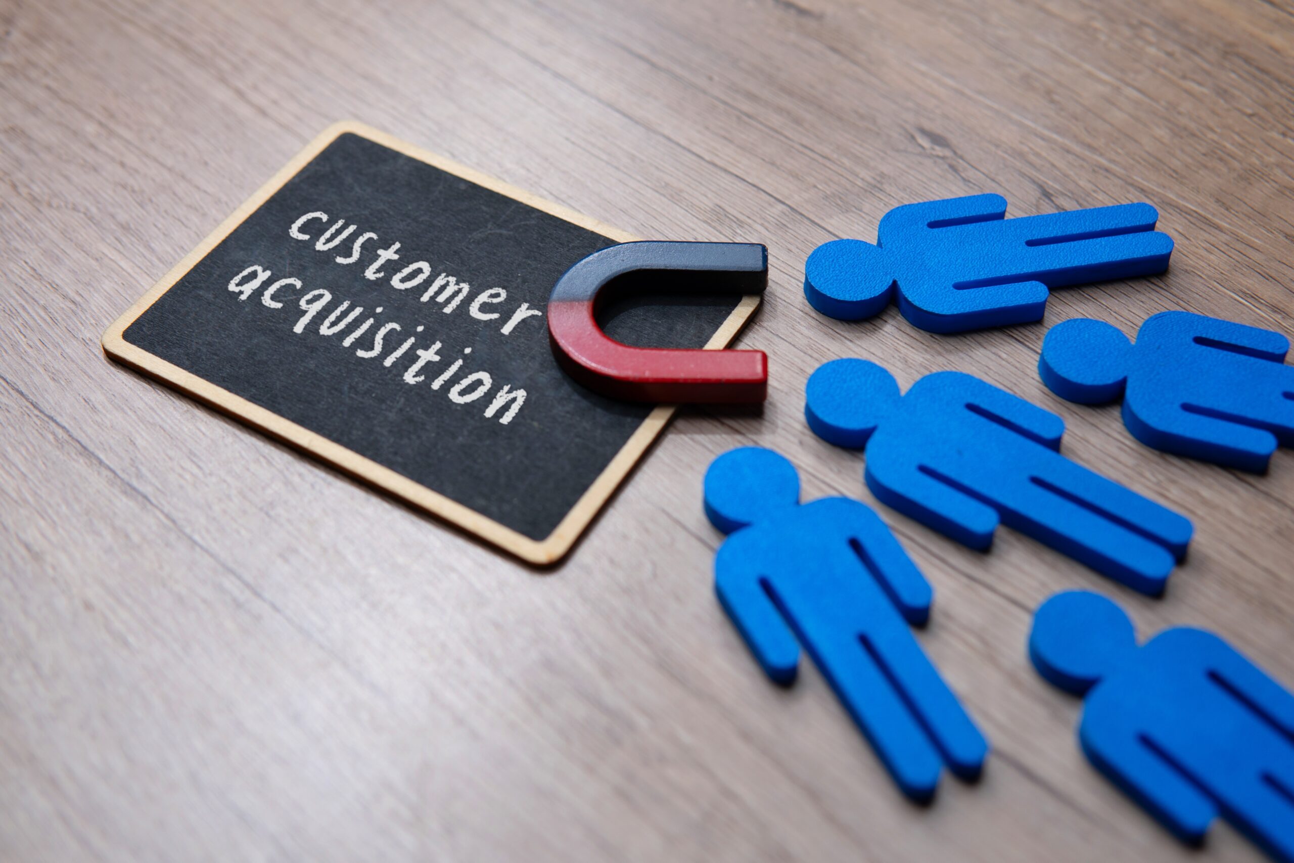 A chalkboard with the words customer acquisition with a magnet and figures